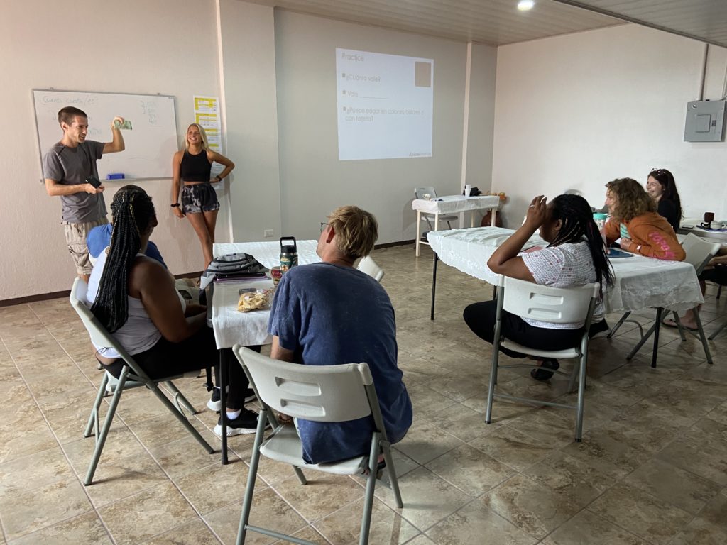 adult students sit around tables watching a teacher