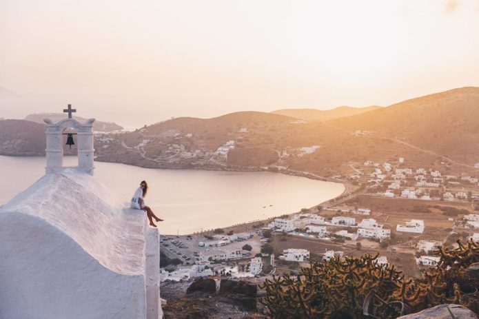 Girl sitting on Greek church looking over beautiful sunset.