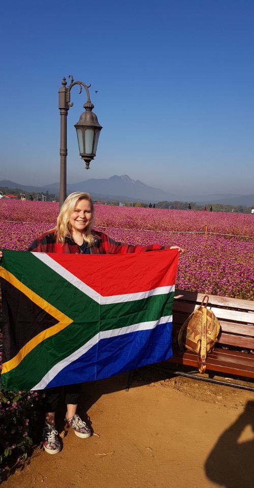 woman holds South African flag in flower field