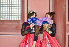 two women in hanbok hiding behind fans