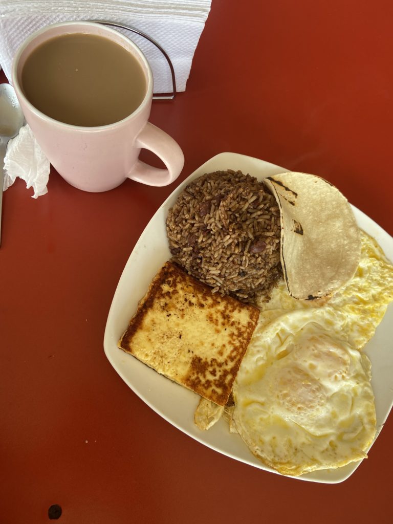 plate with gallo pinto, fried cheese, eggs, and tortillas sitting next to a cup of coffee