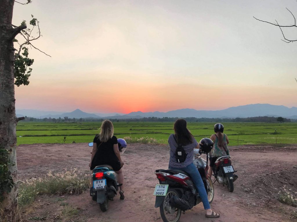 sunset over mountains in thailand and people on scooters